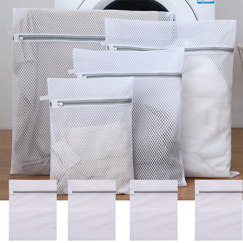 White reusable mesh laundry bags with silver zippers stacked on a wooden surface.