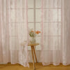 Pink ruffled French lace sheer curtains with floral embroidery hanging in a window.