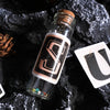 A glass bottle filled with alphabet stickers is displayed on a dark surface next to a white card.