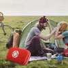 A person is opening a red portable first aid kit with a hard shell case outdoors on grass.