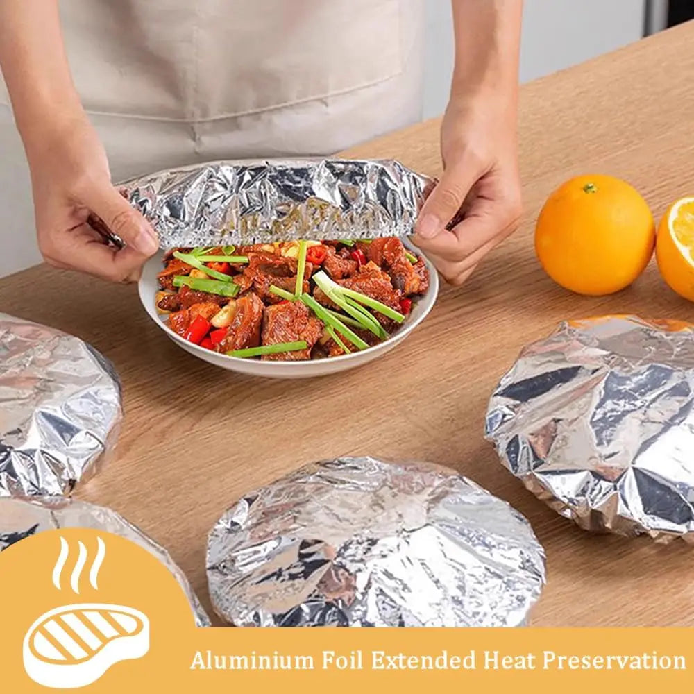 Hände halten eine silberne Aluminiumfolie über ein Teller mit gegartem Fleisch auf einem Holztable.