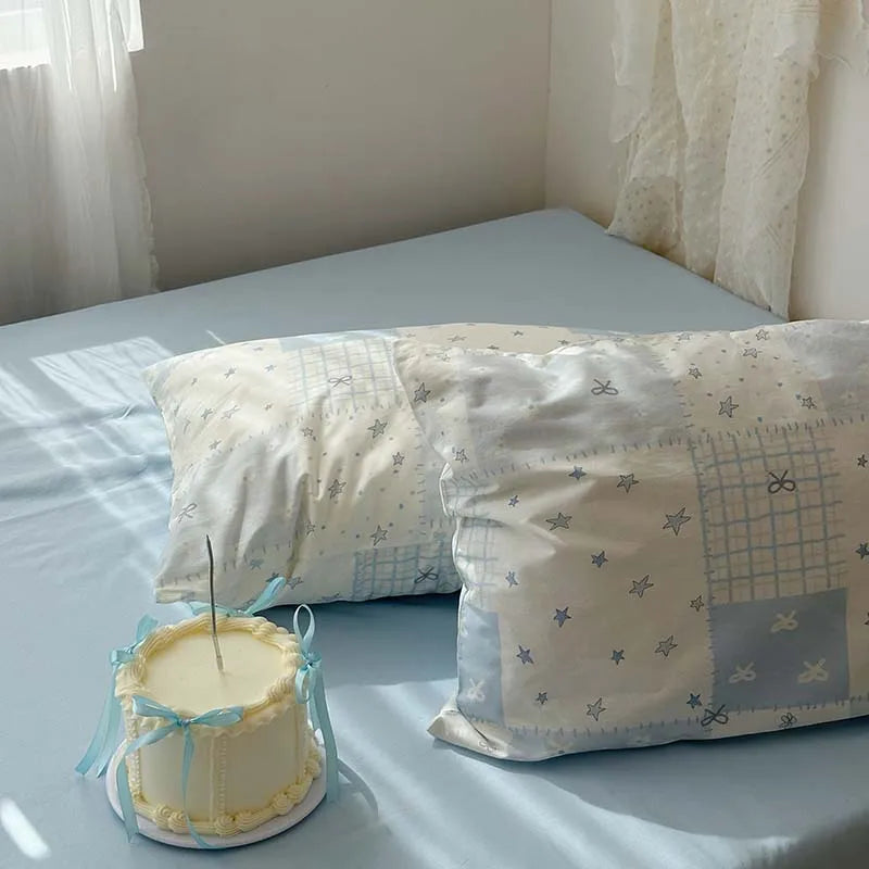 A white cake sits on a blue duvet cover with two patterned pillows.