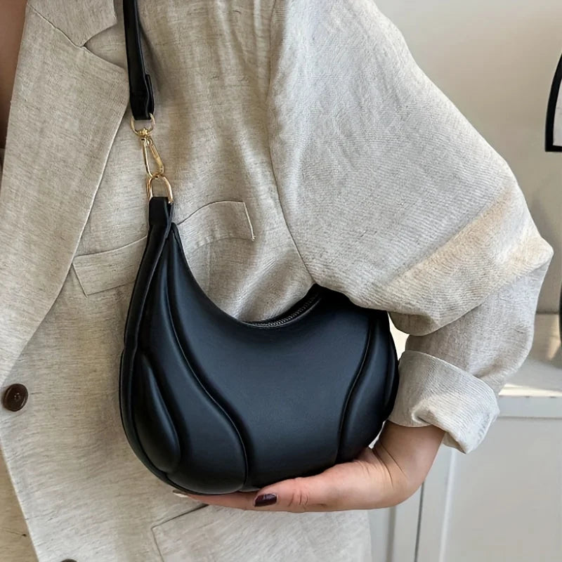 A black textured crossbody bag with a gold-toned strap is held against a light beige blazer.