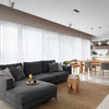 Modernes Wohnzimmer mit grauem Sofa und Holzmöbel vor durchscheinenden weißen Tüllvorhängen.