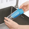 A hand is holding a blue double-sided kitchen scouring sponge over a black sink.