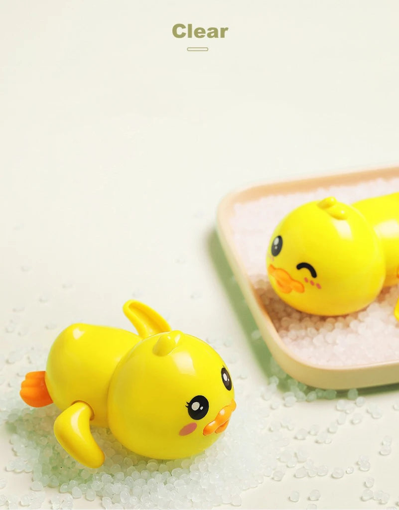 A bright yellow wind-up bath toy duck is resting on white granular material in a light pink dish.