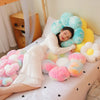 A person is lying on a bed surrounded by numerous soft, fluffy sunflower-themed plush pillows in pink, yellow, and white.