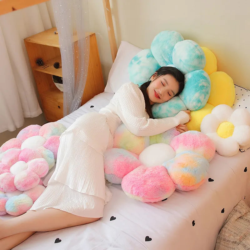 A person is lying on a bed surrounded by numerous soft, fluffy sunflower-themed plush pillows in pink, yellow, and white.