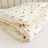 A stack of white muslin baby blankets with small black floral patterns folded on a white surface.