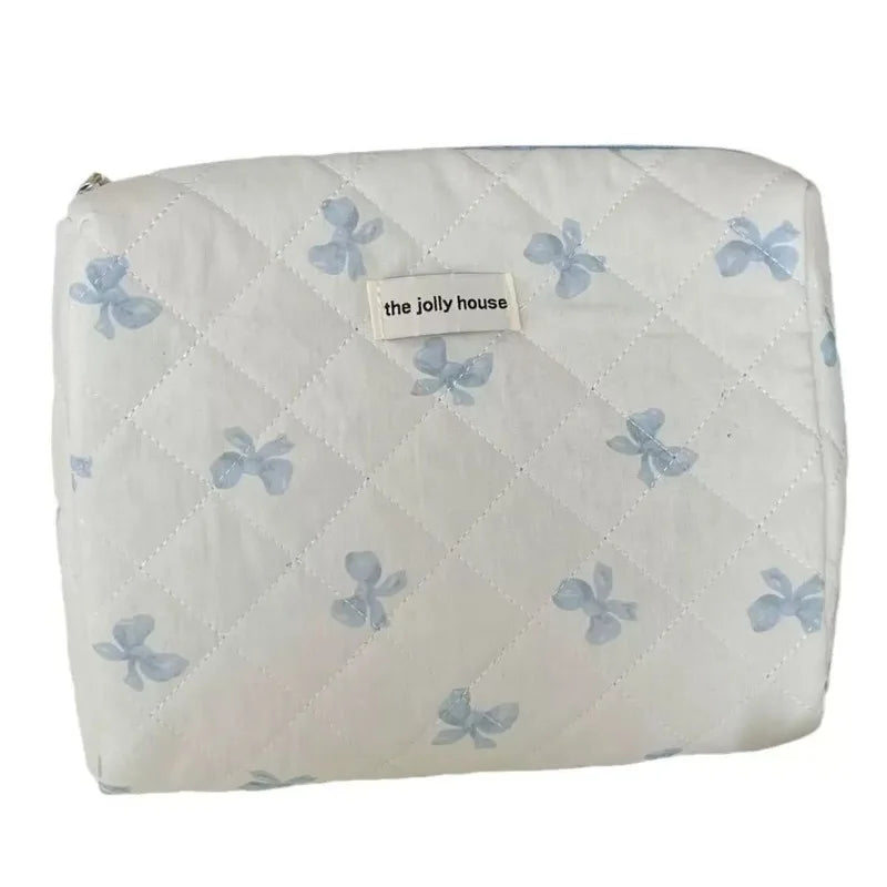 A white quilted cosmetic bag with light blue bow print and a small label reading the jolly house.