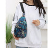 A woman wearing a light gray sweatshirt holds a colorful leaf print sling crossbody bag.