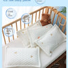White ice silk baby pillow with a teddy bear and a small quilted pattern resting on a wooden crib railing.
