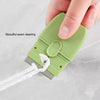 A hand is holding a light green double-ended cleaning scraper with a protective cover, demonstrating seam cleaning.
