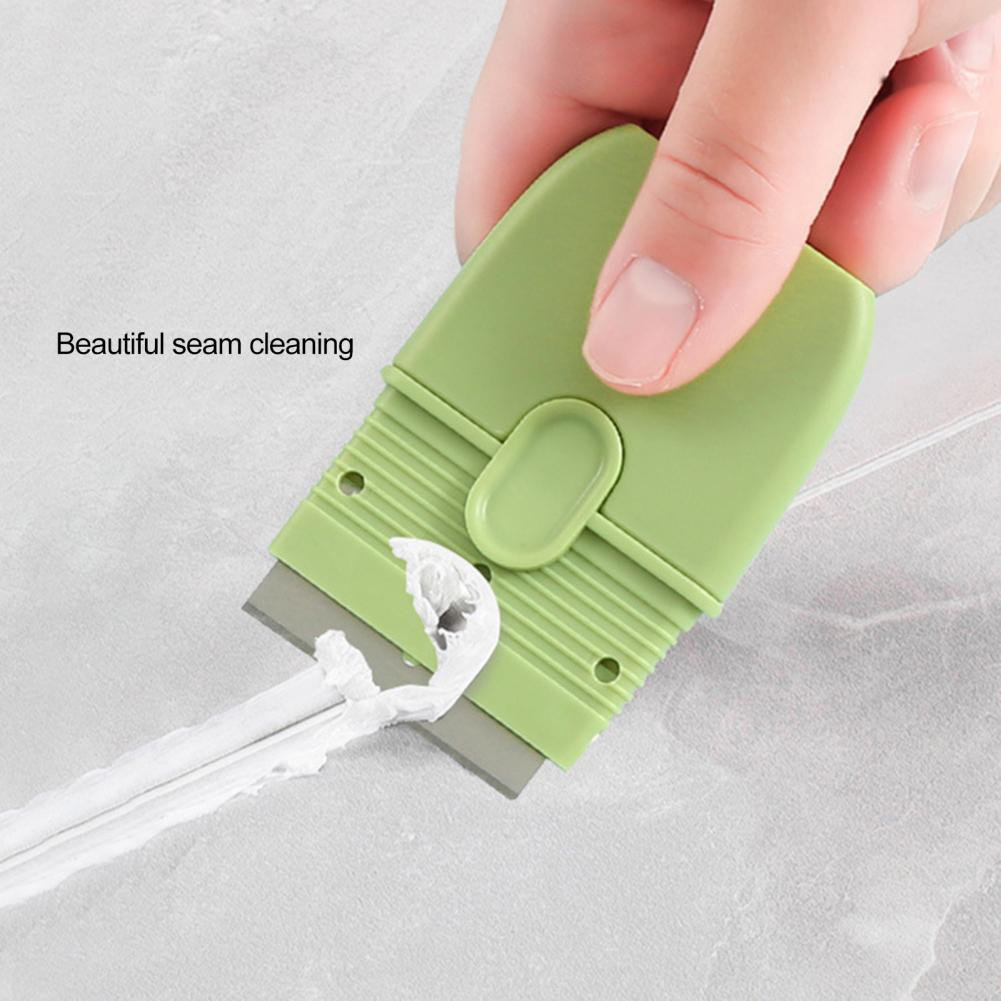 A hand is holding a light green double-ended cleaning scraper with a protective cover, demonstrating seam cleaning.
