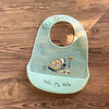 A light green silicone baby bib featuring a cartoon yellow truck and stop sign on a wooden surface.