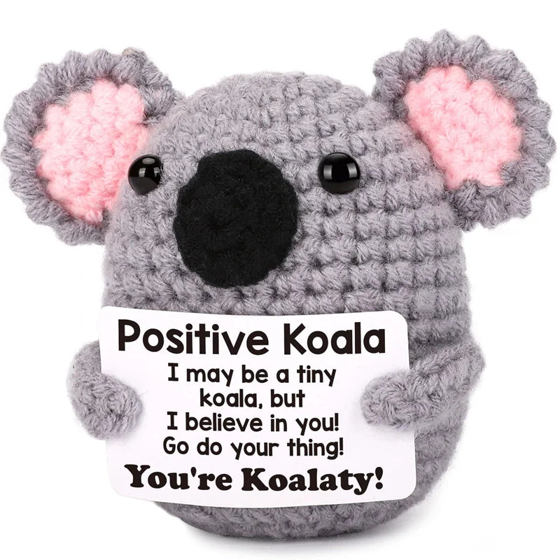 A gray crochet koala plush toy with pink inner ears and a card that reads Positive Koala