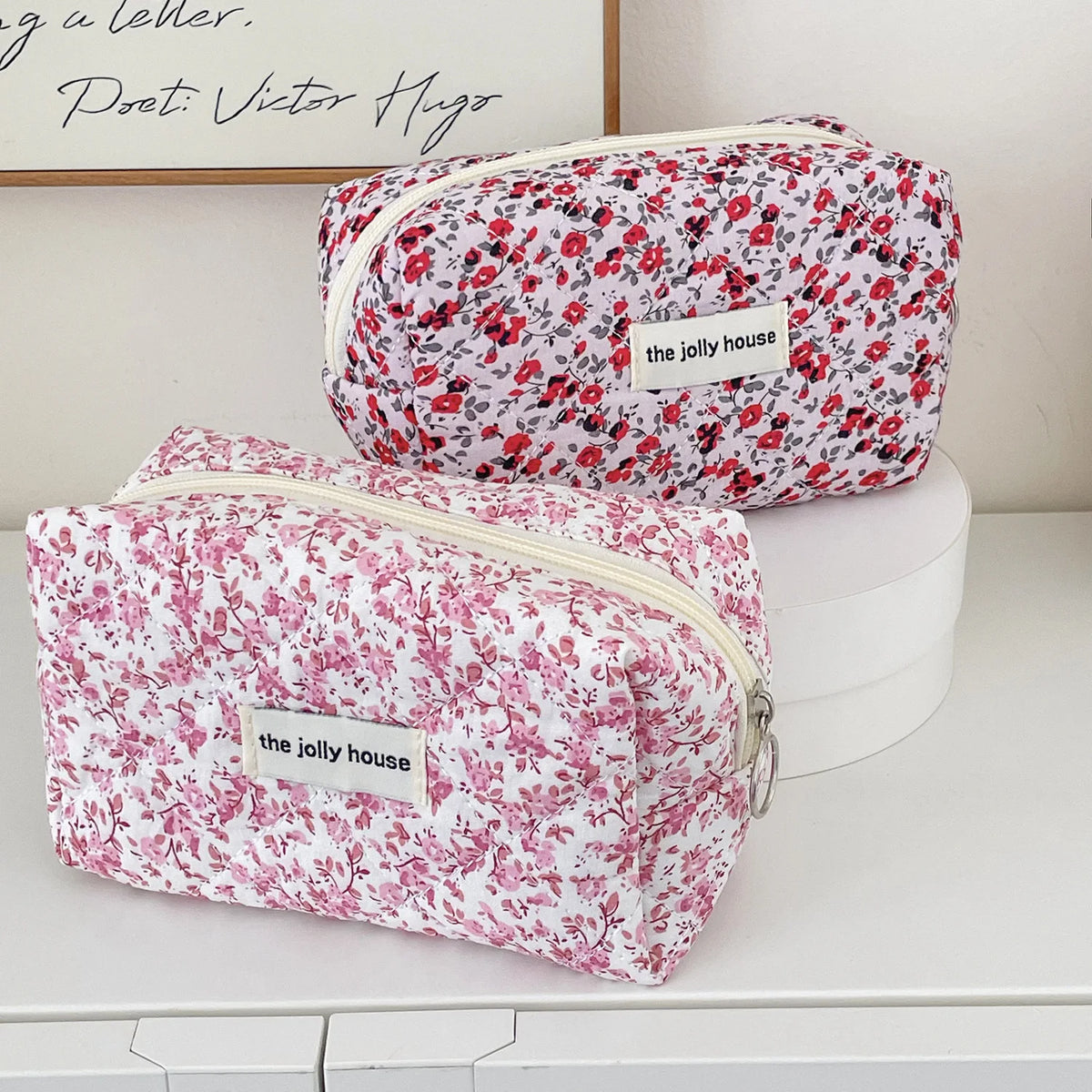 A pink floral quilted makeup bag with a zipper closure resting on a white surface.