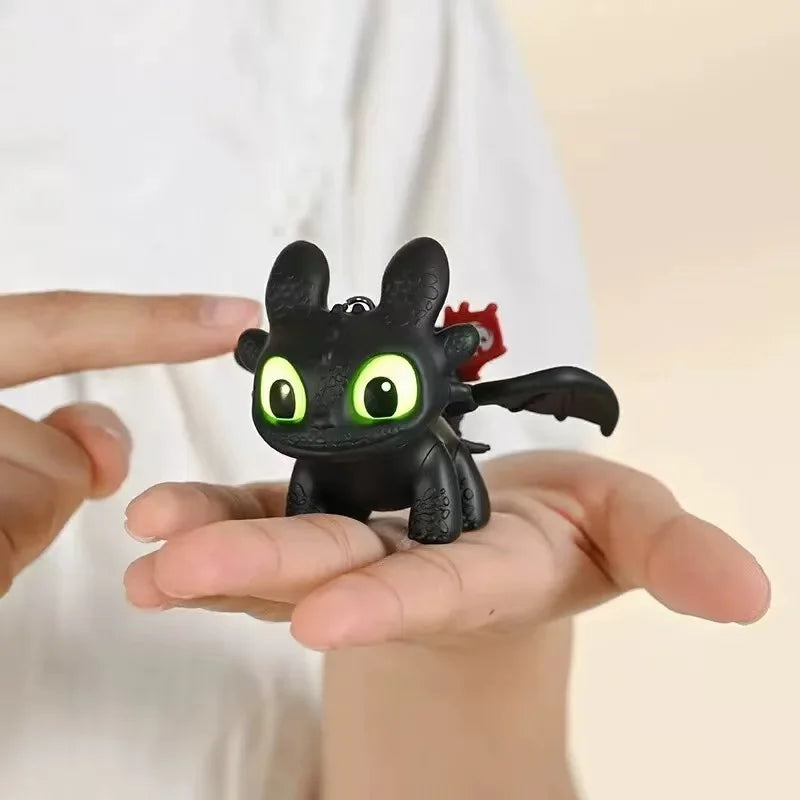A black Toothless car ornament with glowing green eyes and movable wings is held in a person's hand.