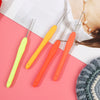 A set of four precision crochet hooks in yellow, orange, and coral colors displayed on pink paper.