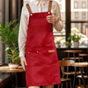 A woman wearing a red polyester kitchen apron over a white shirt stands in a modern indoor setting.