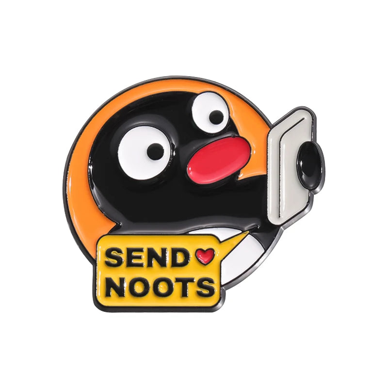 A black and orange cartoon penguin enamel pin with a yellow banner that reads SEND NOOTS