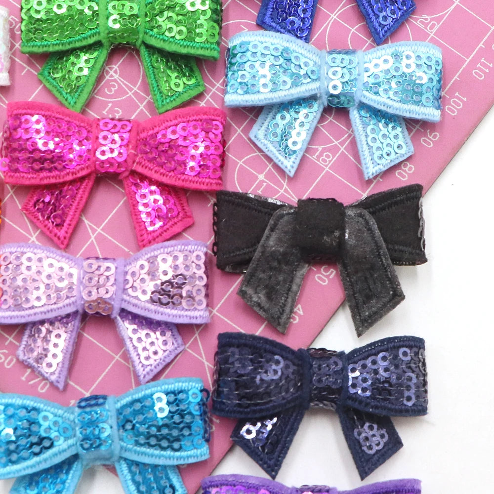 A collection of five sparkly sequin bow patches in various colors including green pink purple blue and black