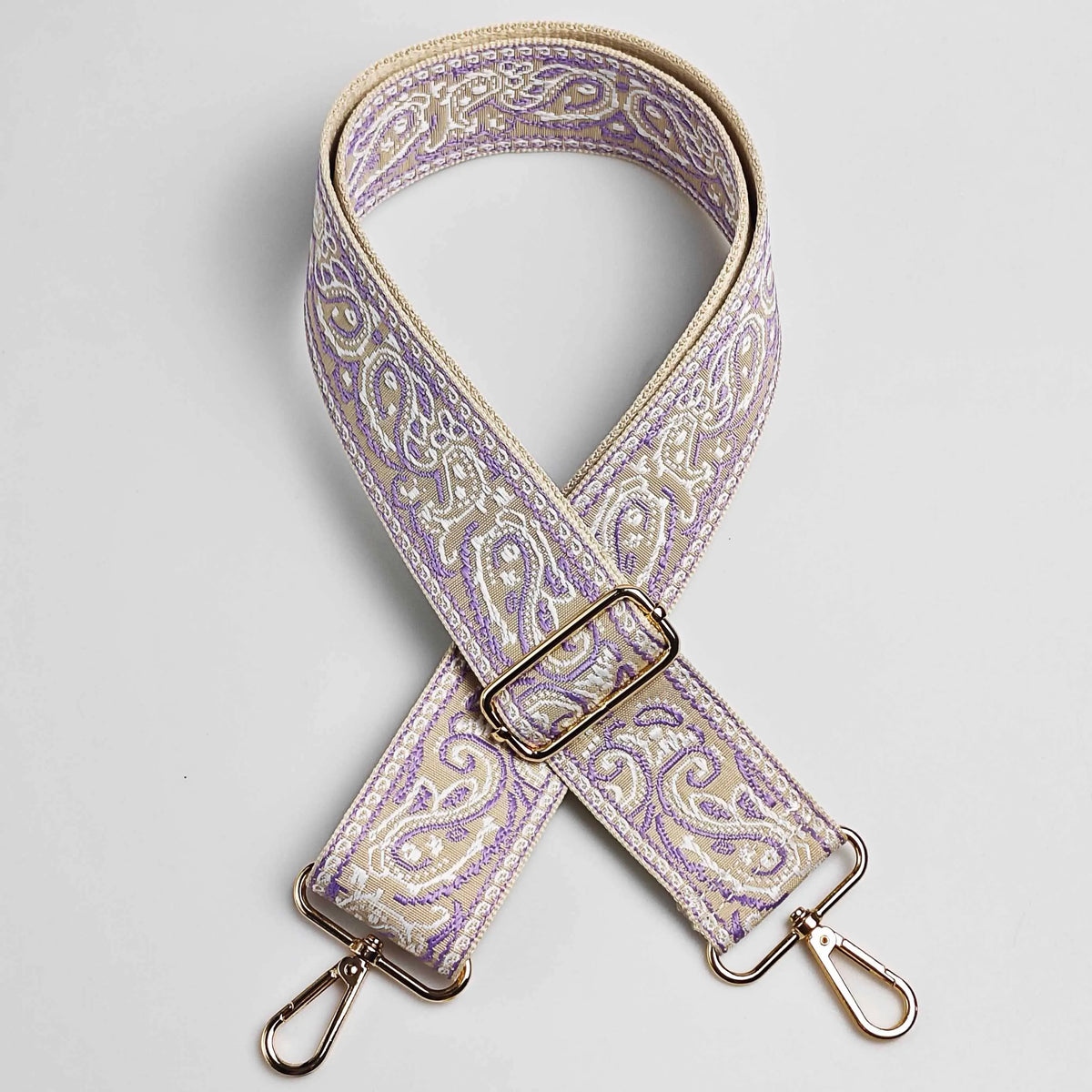 A beige and purple paisley jacquard bag strap with gold hardware.
