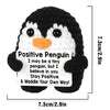A black and white crocheted penguin toy with a positive message card attached.