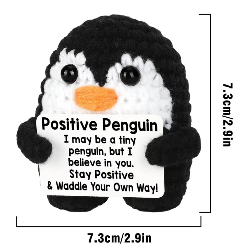 A black and white crocheted penguin toy with a positive message card attached.
