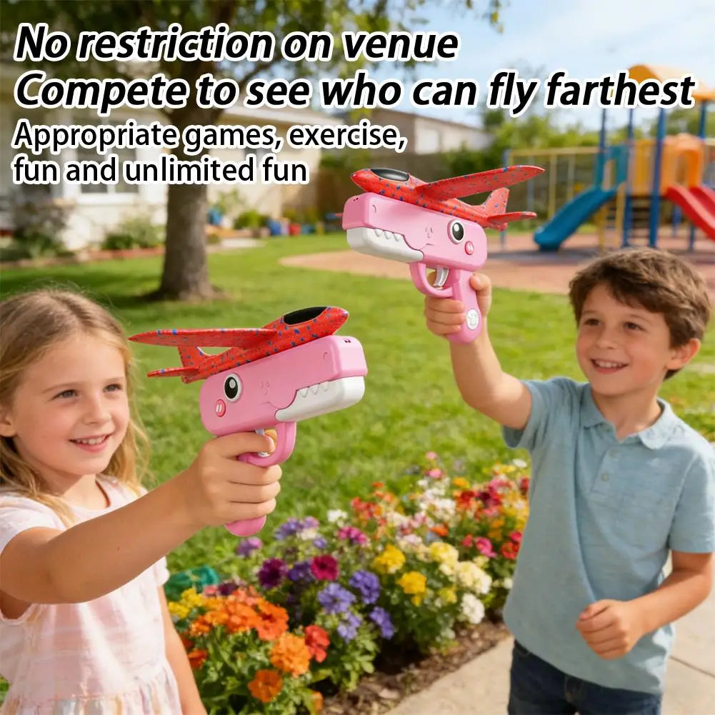 Two children are playing with pink foam catapult airplane toys outdoors in a garden setting.