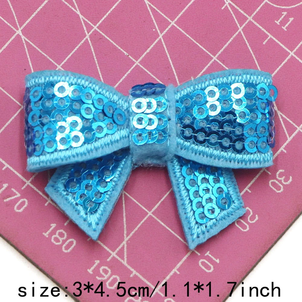 A set of five blue and silver sequin bow patches for DIY crafts displayed on a pink grid background.
