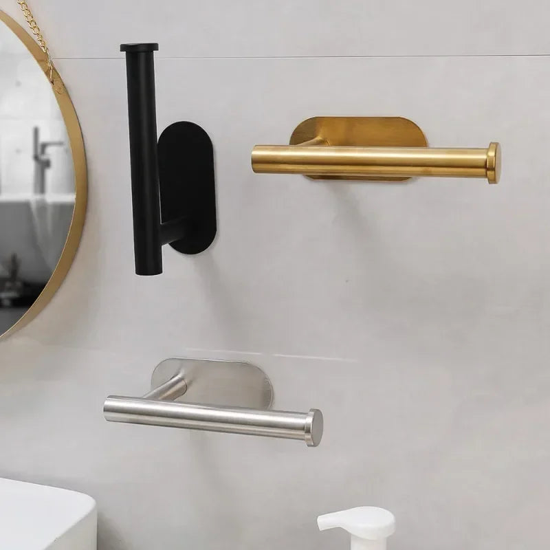 A close-up of a stainless steel self-adhesive toilet paper holder mounted on a white wall.