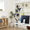 A black adjustable swing arm desk lamp is positioned over a white desk in a bright office setting.