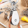 A close-up of a stainless steel swivel pulley with a hook and cord resting on burlap fabric.