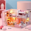 A pink wooden dollhouse miniature building kit with furniture displayed on a light pink surface.