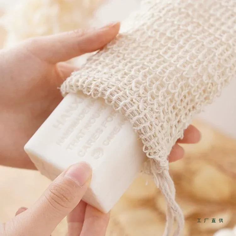 A hand is holding a natural sisal soap saver bag with an exfoliating mesh and a white bar of soap.