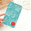 A teal patterned card holder with a round red accent is held against a white background.
