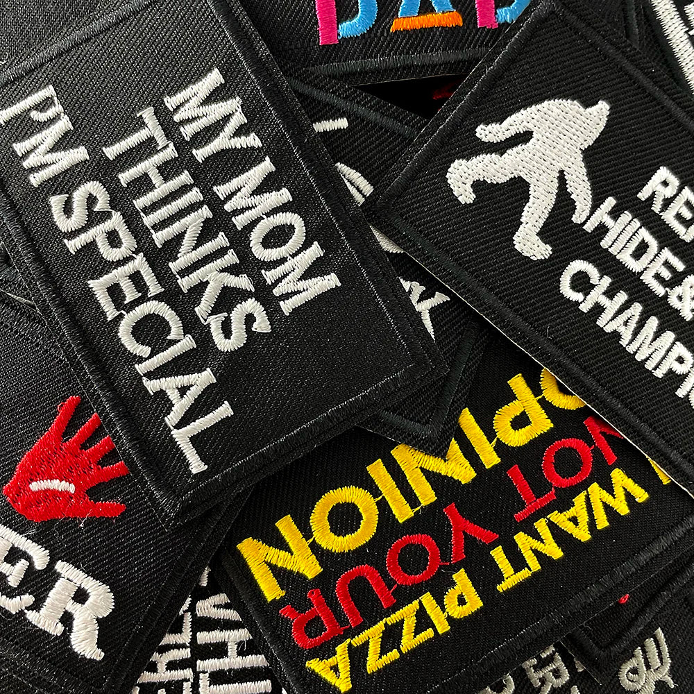 A collection of black embroidered iron-on patches featuring text like MY MOM THINKS SPECIAL and OPTION YOUR OWN PIZZA