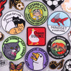 A collection of embroidered iron-on patches featuring funny cartoon and animal designs like a cat lady, a red fish, and a pan