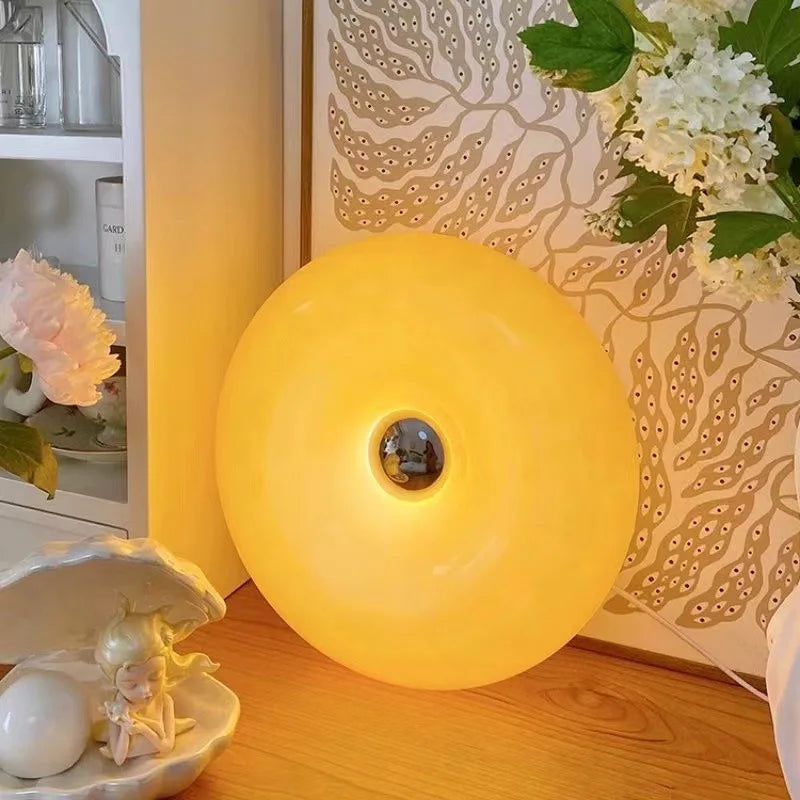 A round, glowing yellow LED wall sconce with a textured pattern on the wall and a white decorative object nearby.