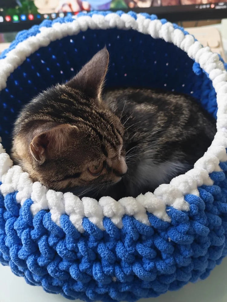 A small tabby kitten is nestled inside a blue and white crocheted pot.