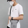 A person wearing a black cap and face mask holds a gray mini crossbody phone bag with an adjustable strap.