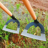 A pair of black and silver handheld weeding rakes with orange handles resting in green grass.