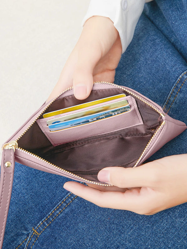 A hand is holding a pink slim PU leather zip-around wallet with card and phone pockets against blue denim fabric.