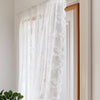 White sheer lace curtains hanging in a wooden frame on a light-colored wall.