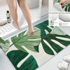 A tropical green leaf print non-slip area rug is shown on a floor, with a person's legs standing nearby.