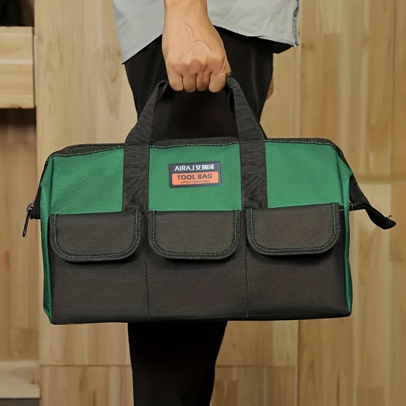 A dark green tool bag with black trim and multiple pockets is held by a person against a light wooden background.