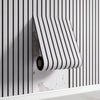 A roll of striped white and black self-adhesive wall panels mounted on a white shelf against a vertically striped wall.