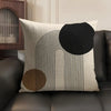 A beige linen cushion cover featuring black geometric lines and circles on a dark brown leather sofa.
