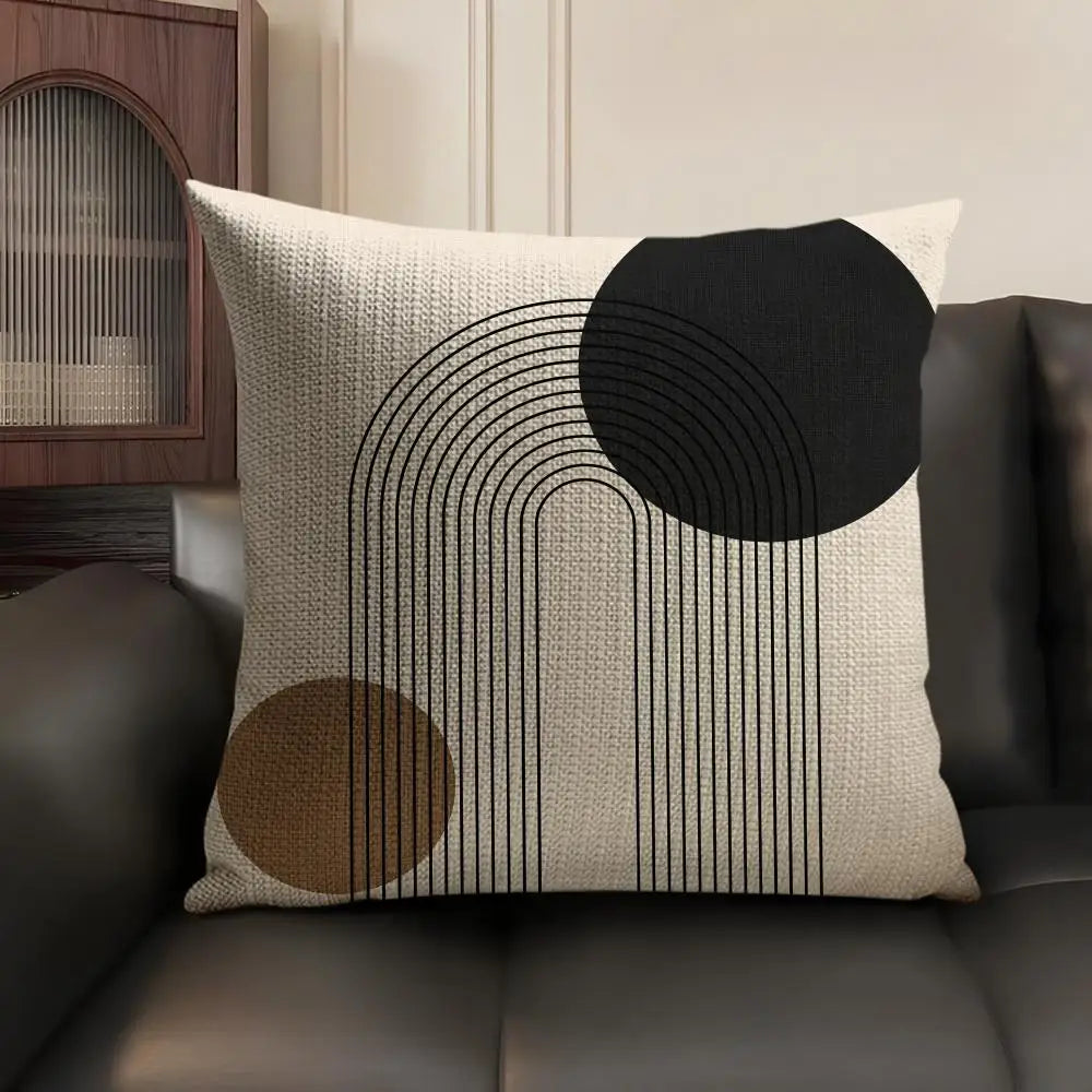 A beige linen cushion cover featuring black geometric lines and circles on a dark brown leather sofa.